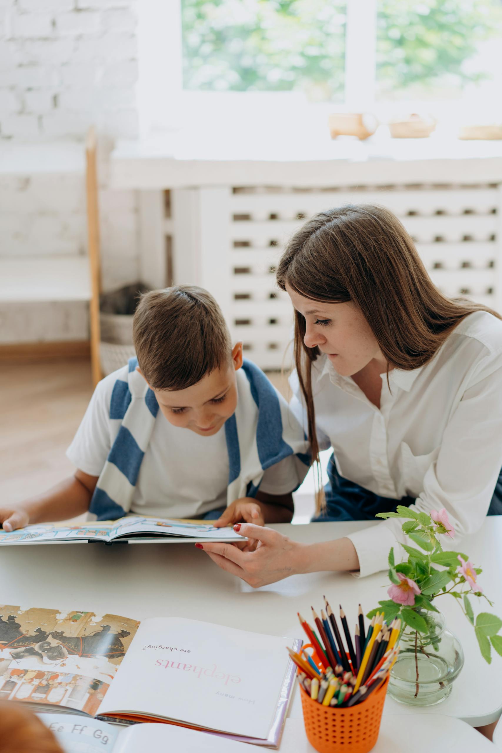 A mother and her son enjoy reading a book together in a sunny, cozy room.