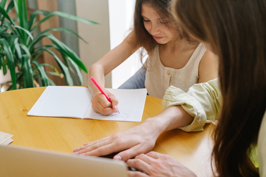 A woman helping a young girl with a writing task at a wooden table, enhancing their learning experience.