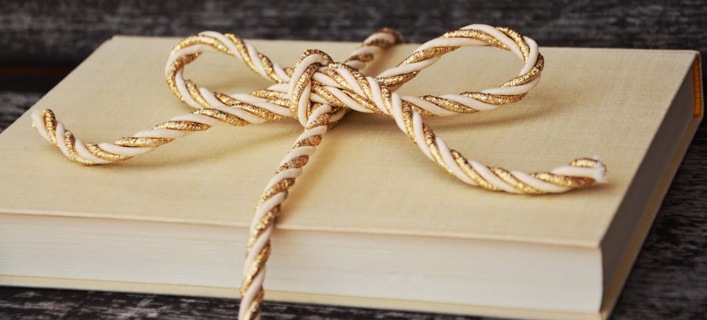 An elegantly wrapped book with a gold and white twisted ribbon, perfect for gifting.