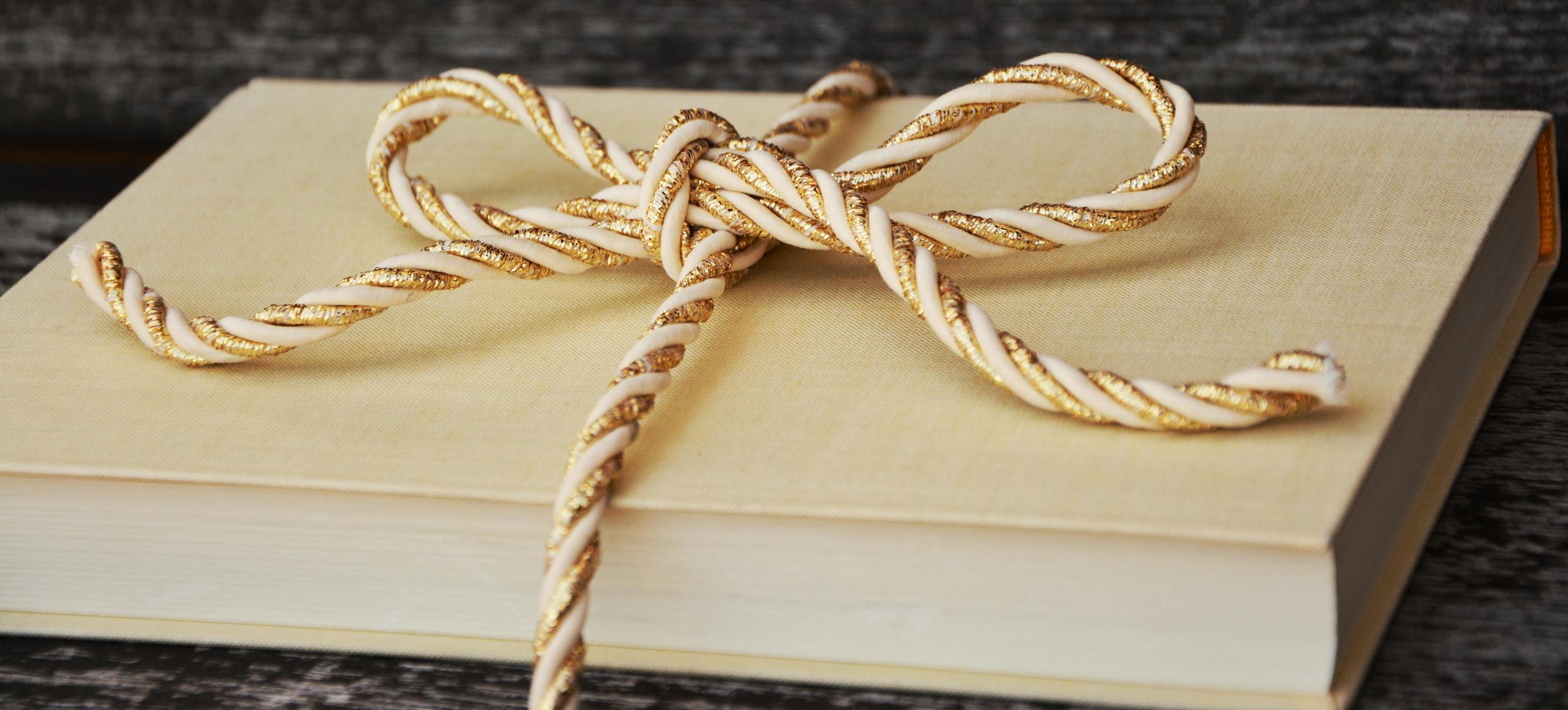 An elegantly wrapped book with a gold and white twisted ribbon, perfect for gifting.